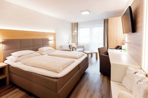 Habitación de hotel con una cama grande, un escritorio, una silla, un televisor y un área de baño.