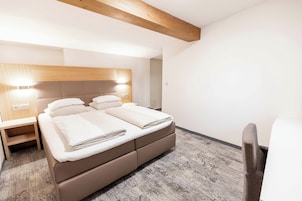 Habitación de hotel con una cama, mesitas de noche, una silla y una viga de techo de madera.