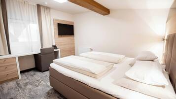 A hotel room with a bed, a desk, a chair, a TV mounted on the wall, and a window with curtains.