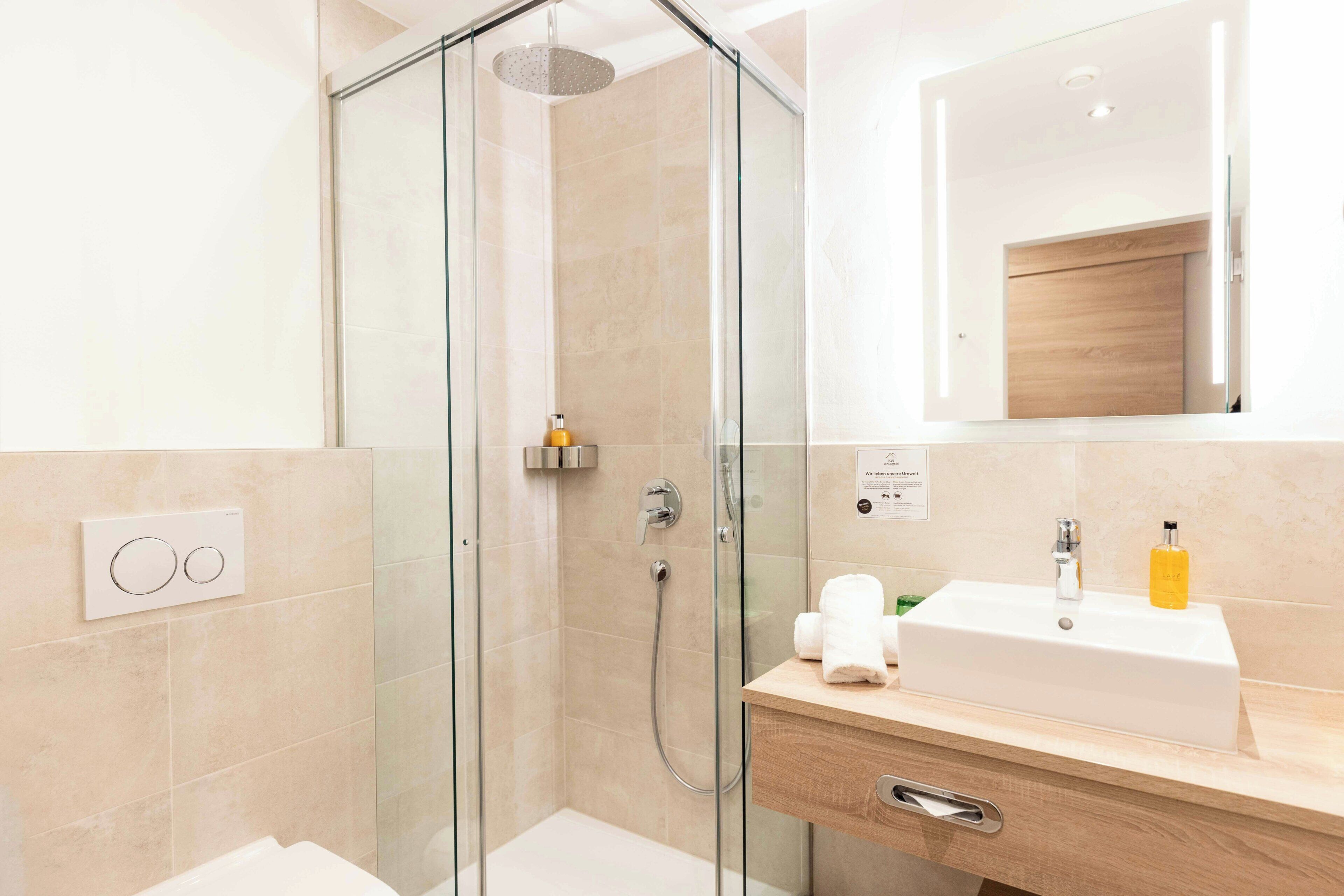 A modern bathroom with a glass-enclosed shower, a white sink with a wooden countertop, and a mirror above the sink.