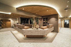 A reception area with a curved wooden ceiling, a central seating arrangement, and a glass partition with a view into another room.
