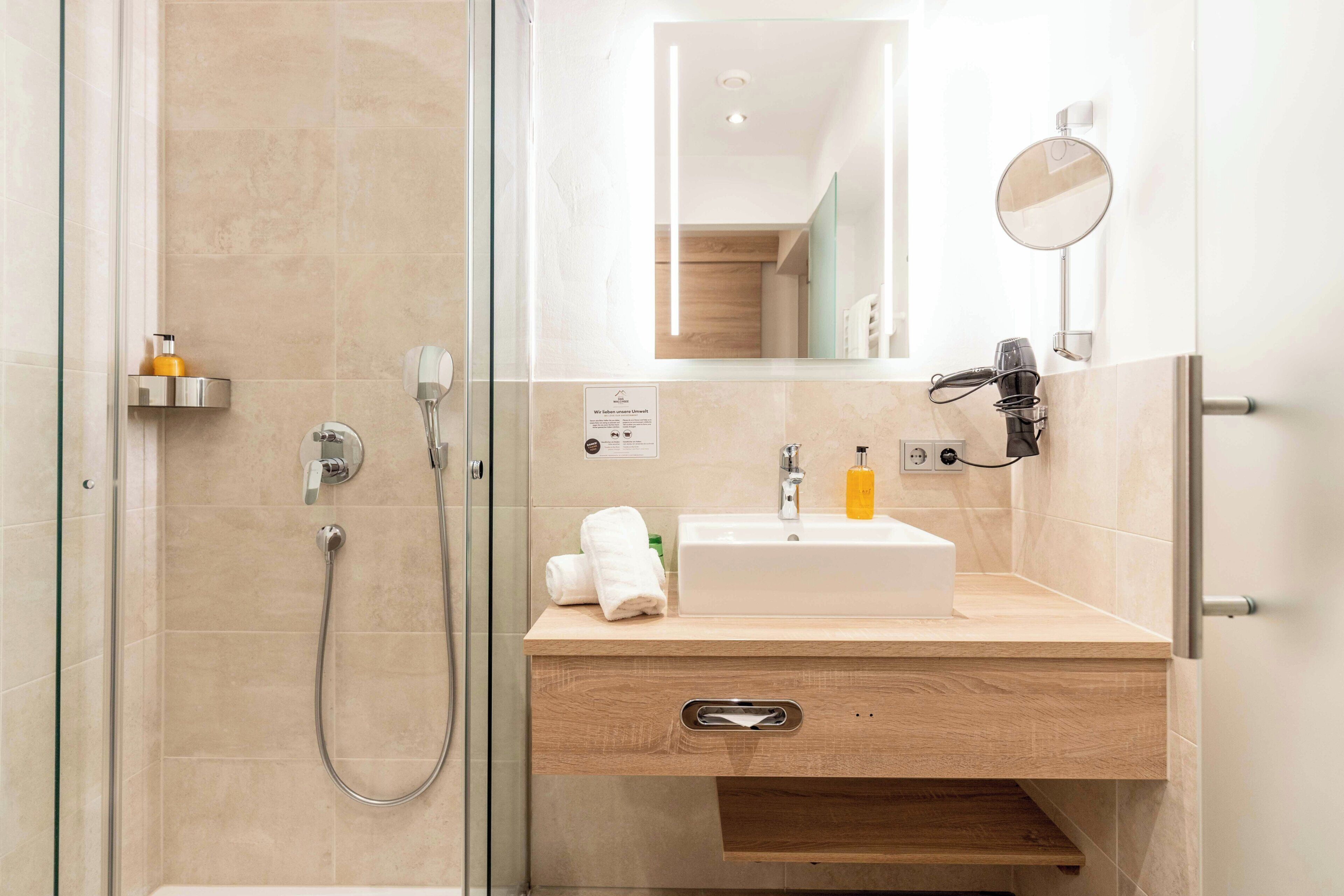 A modern bathroom with a glass shower enclosure, a sink with a mirror, and a hairdryer on the wall.