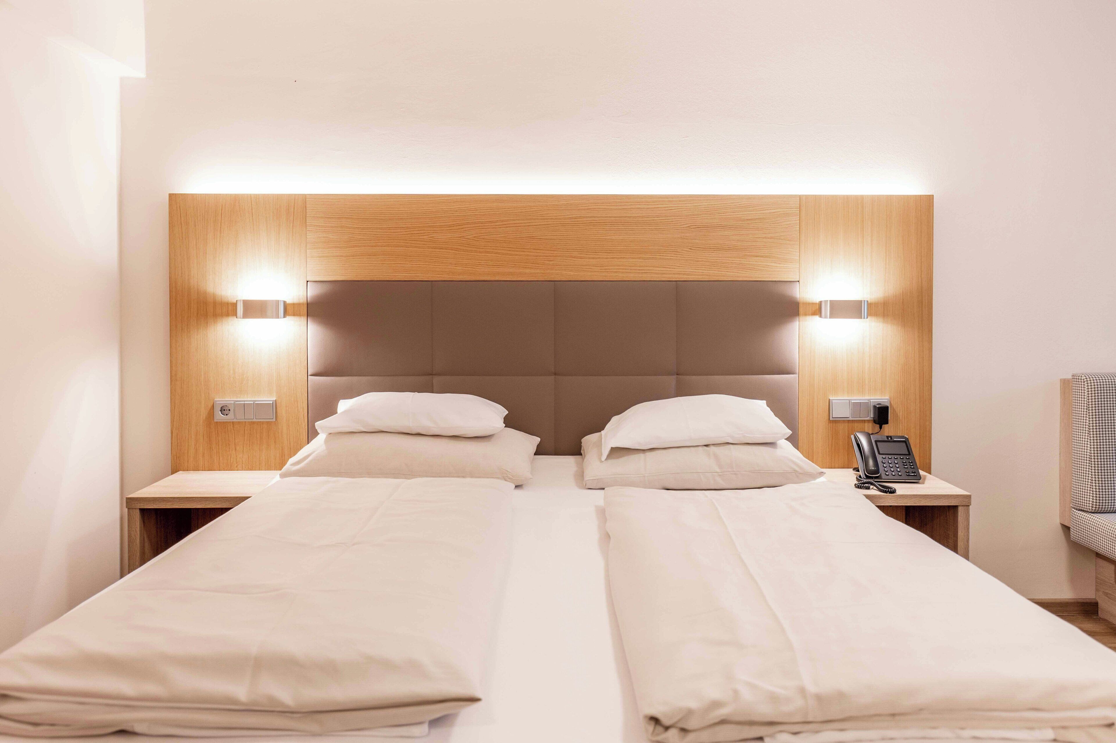 Camera d'albergo con due letti singoli, una testiera in legno, lampade sui comodini, un telefono sul tavolino e un piccolo tavolo.