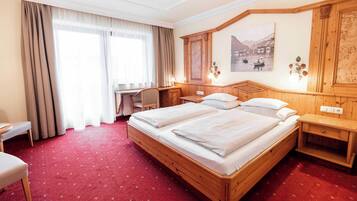 Ein Hotelzimmer mit einem großen Bett, einem Schreibtisch, einem Sessel und Blick auf einen See durch das Fenster.