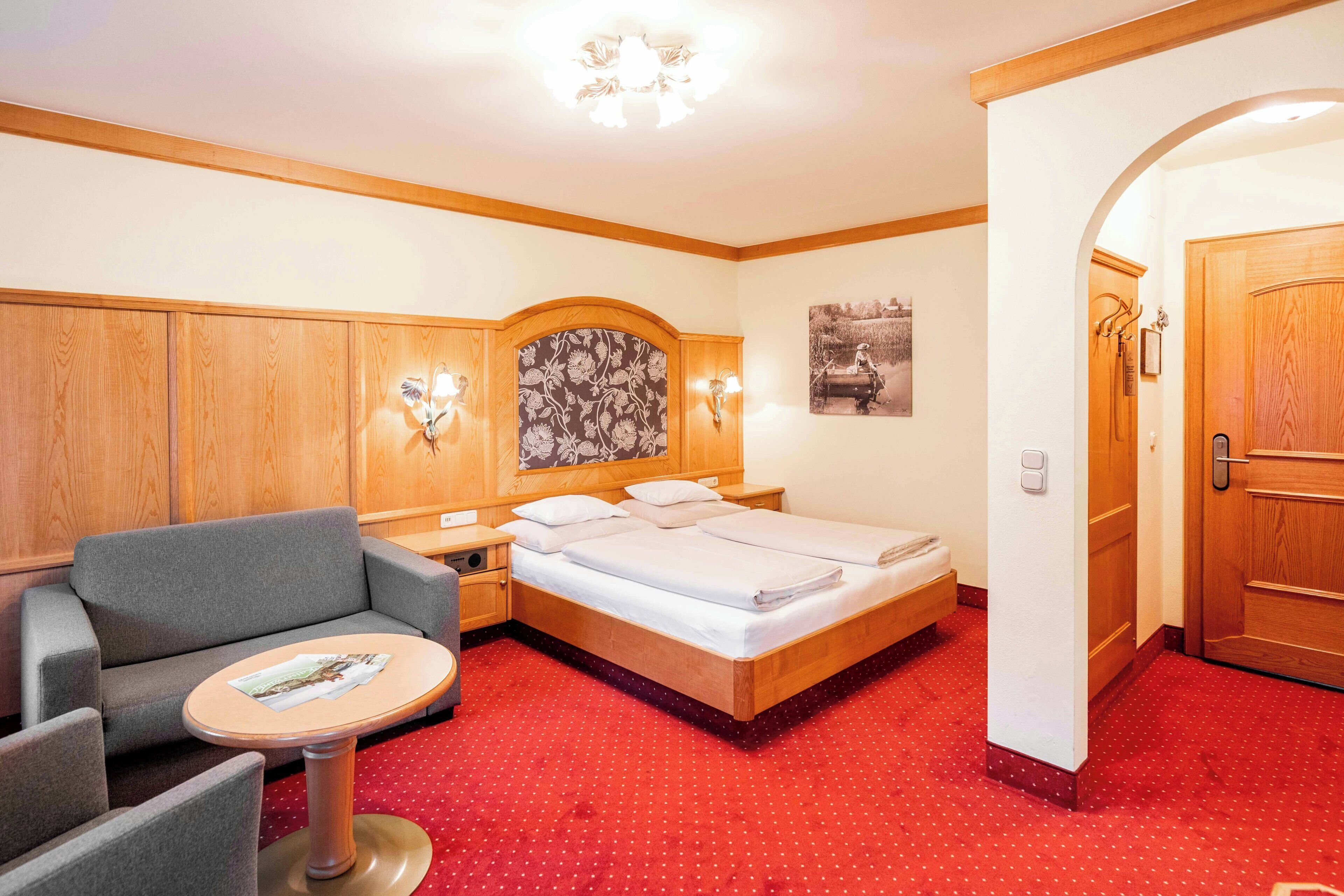 A hotel room with a bed, a sofa, a small table, and a wooden door.