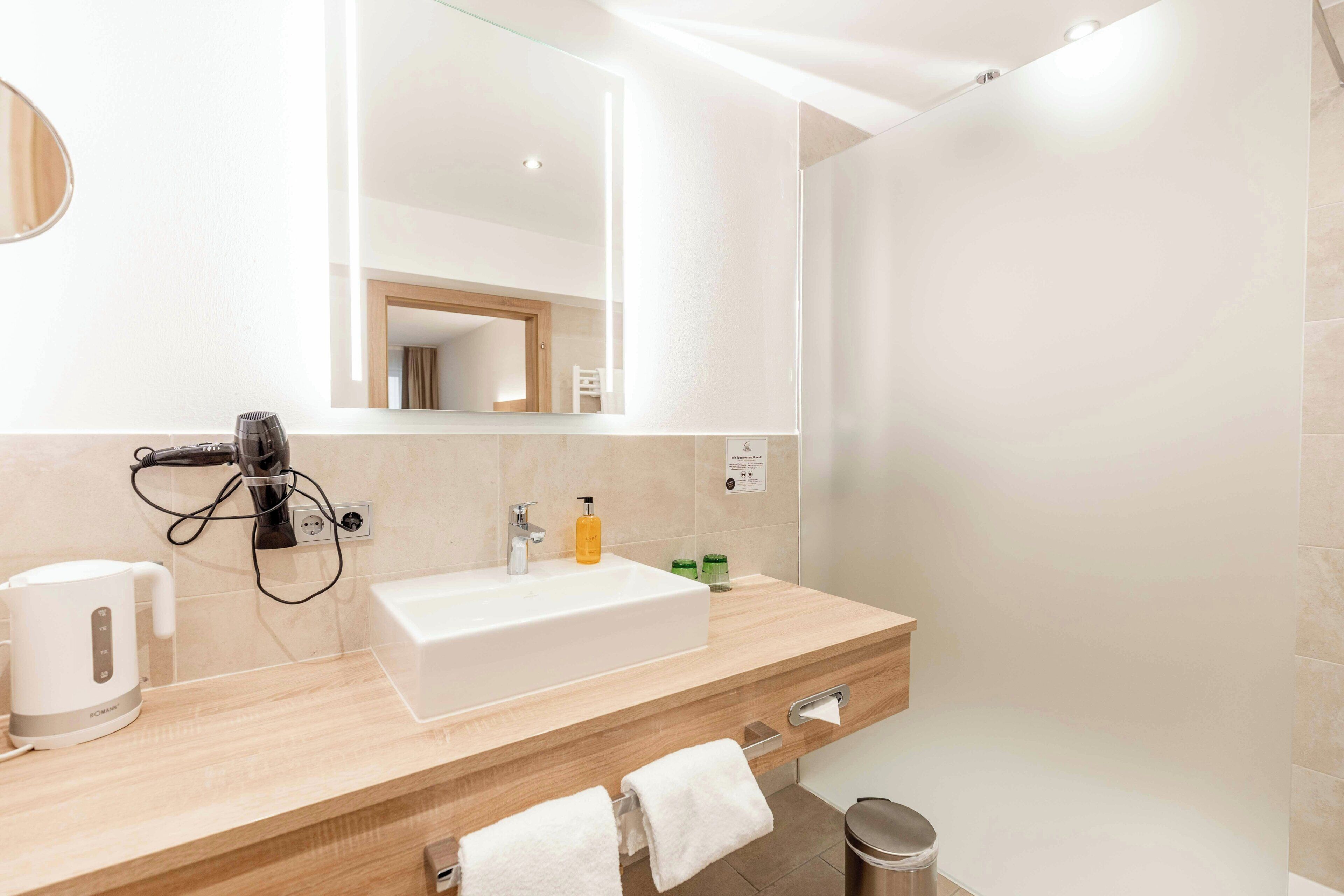 A modern bathroom with a large mirror, a sink, a towel rack, and a trash bin.