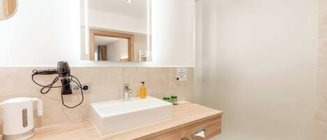 A modern bathroom with a large mirror, a sink, a towel rack, and a trash bin.