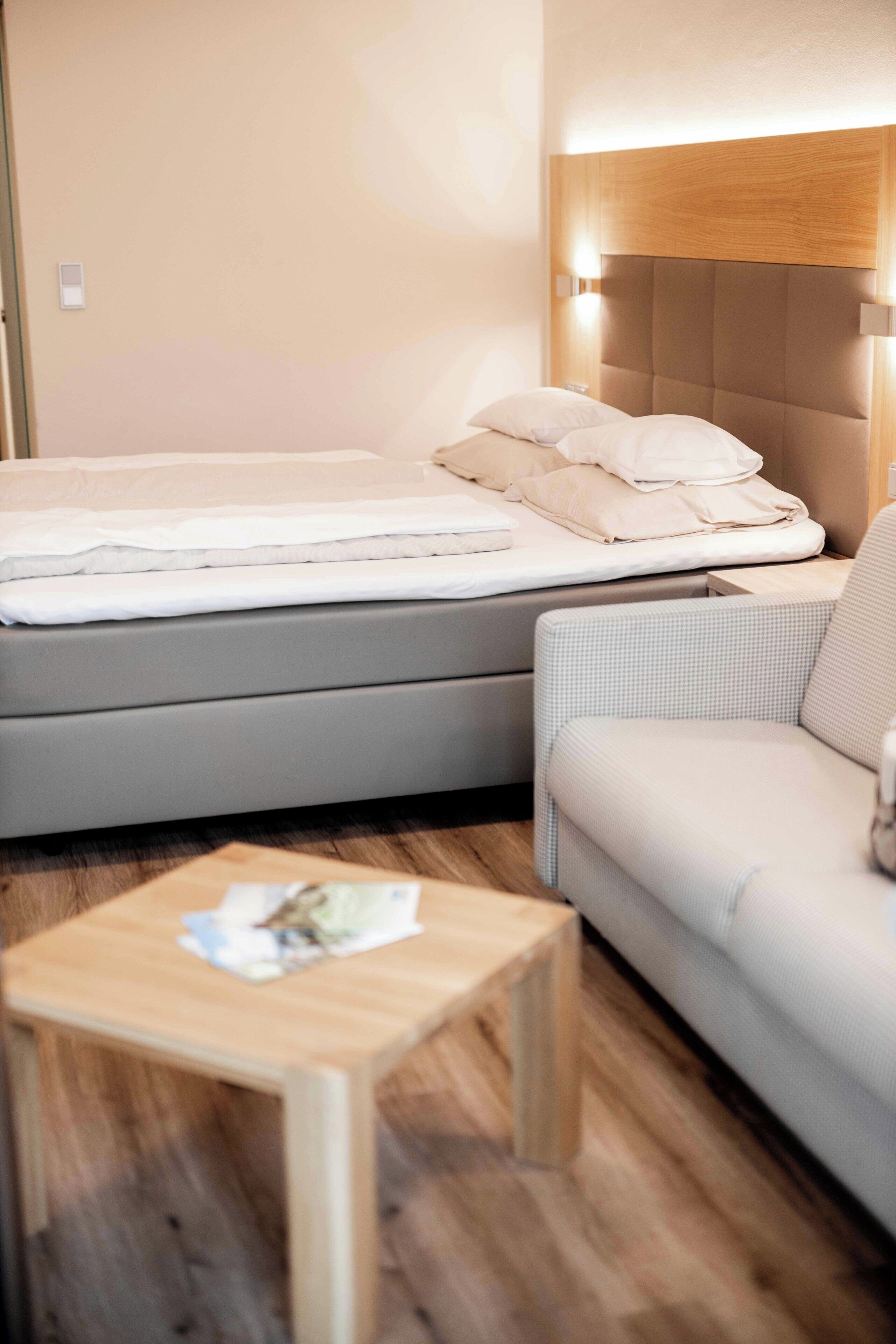 Hotelkamer met twee bedden, een bank, een houten tafel en een hoofdeinde met ingebouwde verlichting.