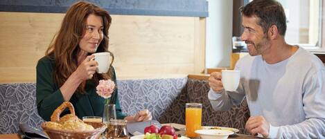 Two people seated at a table with breakfast items, including fruit and a glass of orange juice.