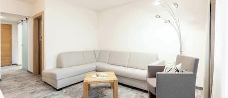 Una sala moderna con un sofá modular, una mesita de madera y un sillón gris.