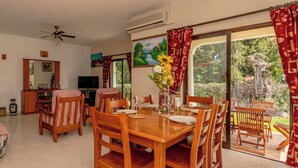 A dining area with a wooden table and chairs, a TV, and a large window with curtains.