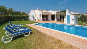 A modern villa with a swimming pool, sun loungers, and a covered patio area.