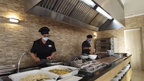 A kitchen with two chefs preparing food, a buffet counter with various dishes, and a brick wall. - Arenas de Son Bou (Alayor)