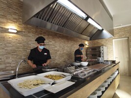 A kitchen with two chefs preparing food, a buffet counter with various dishes, and a brick wall.
