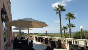 An outdoor patio with tables and chairs, umbrellas, and a view of the sea. - Arenas de Son Bou (Alayor)