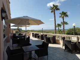 An outdoor patio with tables and chairs, umbrellas, and a view of the sea.