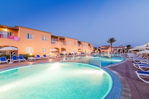 A swimming pool with lounge chairs and umbrellas, surrounded by buildings with balconies and windows.