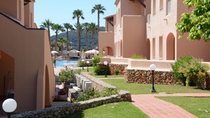 A resort with a swimming pool, palm trees, and a stone pathway. - Arenas de Son Bou (Alayor)