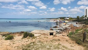 A beach with clear blue water, rocky terrain, and a few people. - Arenas de Son Bou (Alayor)