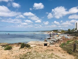 Una playa con agua azul cristalina, terreno rocoso y algunas personas.