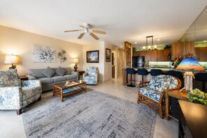 A modern living room with a sofa, armchairs, a coffee table, and a dining area with bar stools.