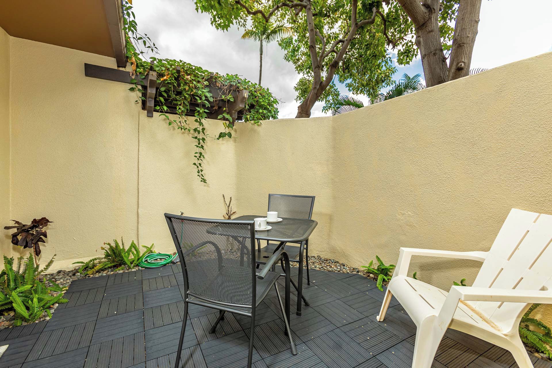 An outdoor patio with a table and chairs, surrounded by plants and a textured wall.