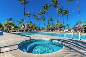 A swimming pool with a hot tub, surrounded by palm trees and lounge chairs.