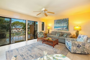 A living room with a sofa, chairs, a coffee table, and a painting of a beach scene.