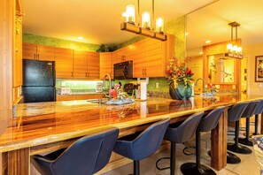 A modern kitchen with wooden cabinets, a black refrigerator, a large island with bar stools, and a hanging light fixture.
