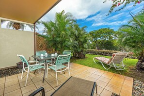 An outdoor patio with a table and chairs, surrounded by lush greenery and palm trees.