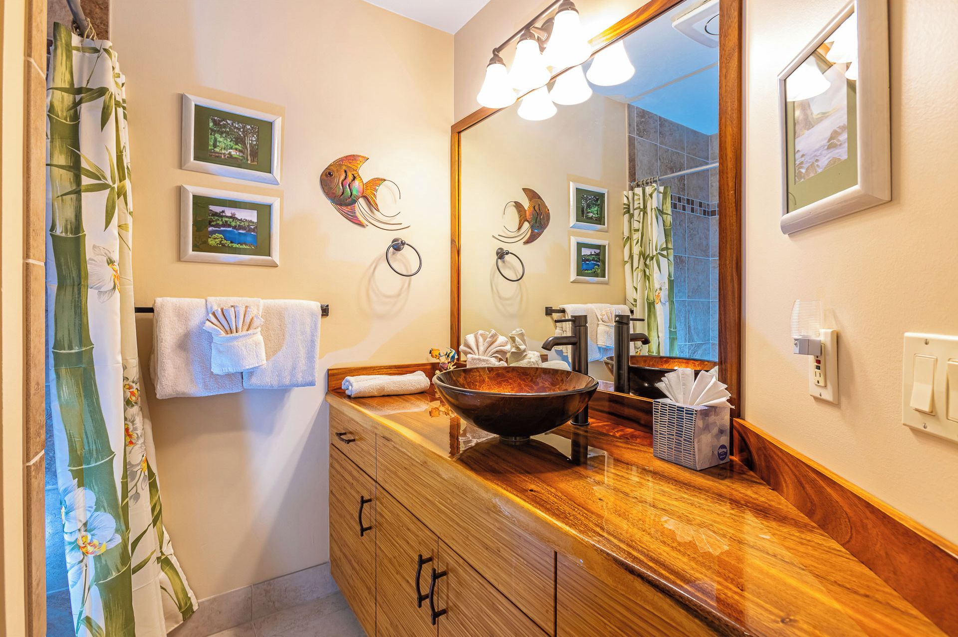 A bathroom with a wooden vanity, a large mirror, and a sink with a bowl basin. There are towels hanging on the wall and a shower curtain with a bamboo design.