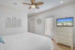 A bedroom with a large bed, a ceiling fan, a dresser, a television, and decorative wall art. - Golf Course Views ~ Golf Cart ~ Community Pool (Miramar Beach)