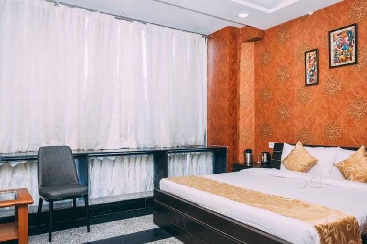Ein Hotelzimmer mit einem großen Bett, einem Sessel, einem Schreibtisch und einem Fenster mit Vorhängen.