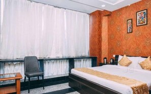 Una habitación de hotel con una cama grande, una silla, un escritorio y una ventana con cortinas.