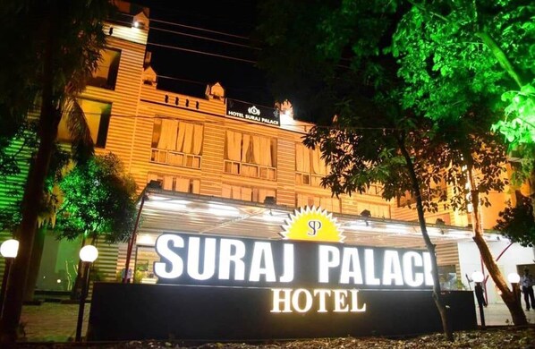 Exterior del Hotel Suraj Palace, con señalización iluminada y un llamativo emblema solar.
