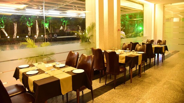 A restaurant with long tables, chairs, and a view of greenery outside. - Hotel Suraj Palace (Bhopal)