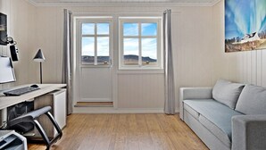 A room with a desk, a computer, a chair, a couch, and a painting of a landscape. - Green Gold of Norway (Lyngen)