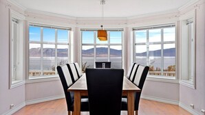 A dining area with a view of mountains and a lake, featuring a wooden table and black chairs. - Green Gold of Norway (Lyngen)