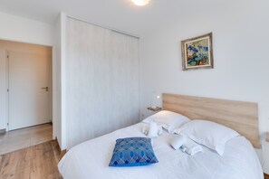 Un lit bien fait, avec du linge de lit blanc et un coussin à motifs bleus, une tête de lit en bois et une petite table de chevet avec une lampe.