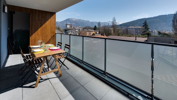A balcony with a table set for dining, overlooking a mountainous landscape with buildings in the background.