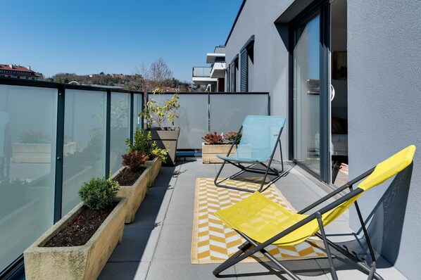 A modern balcony with a yellow chair, a blue chair, and potted plants.