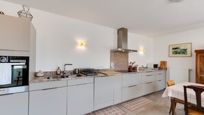 A modern kitchen with a built-in oven, a stainless steel range hood, and a long countertop.