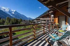 A wooden balcony with a view of snow-capped mountains, a pool, and lounge chairs. - La Cordee 124 Ap - Lakefront - Chamonix All Year (Chamonix-Mont-Blanc)
