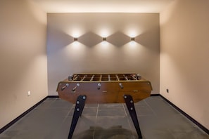 A foosball table in a room with a tiled floor and a wall-mounted light fixture. - La Cordee 124 Ap - Lakefront - Chamonix All Year (Chamonix-Mont-Blanc)