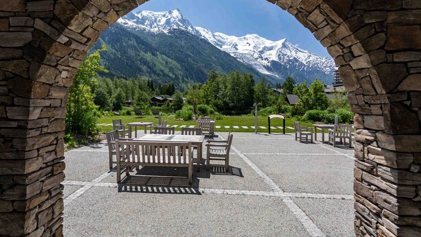 An outdoor seating area with stone walls and a view of snow-capped mountains. - La Cordee 124 Apartment -  an apartment sleeping 6 with parking & pool (Chamonix-Mont-Blanc)