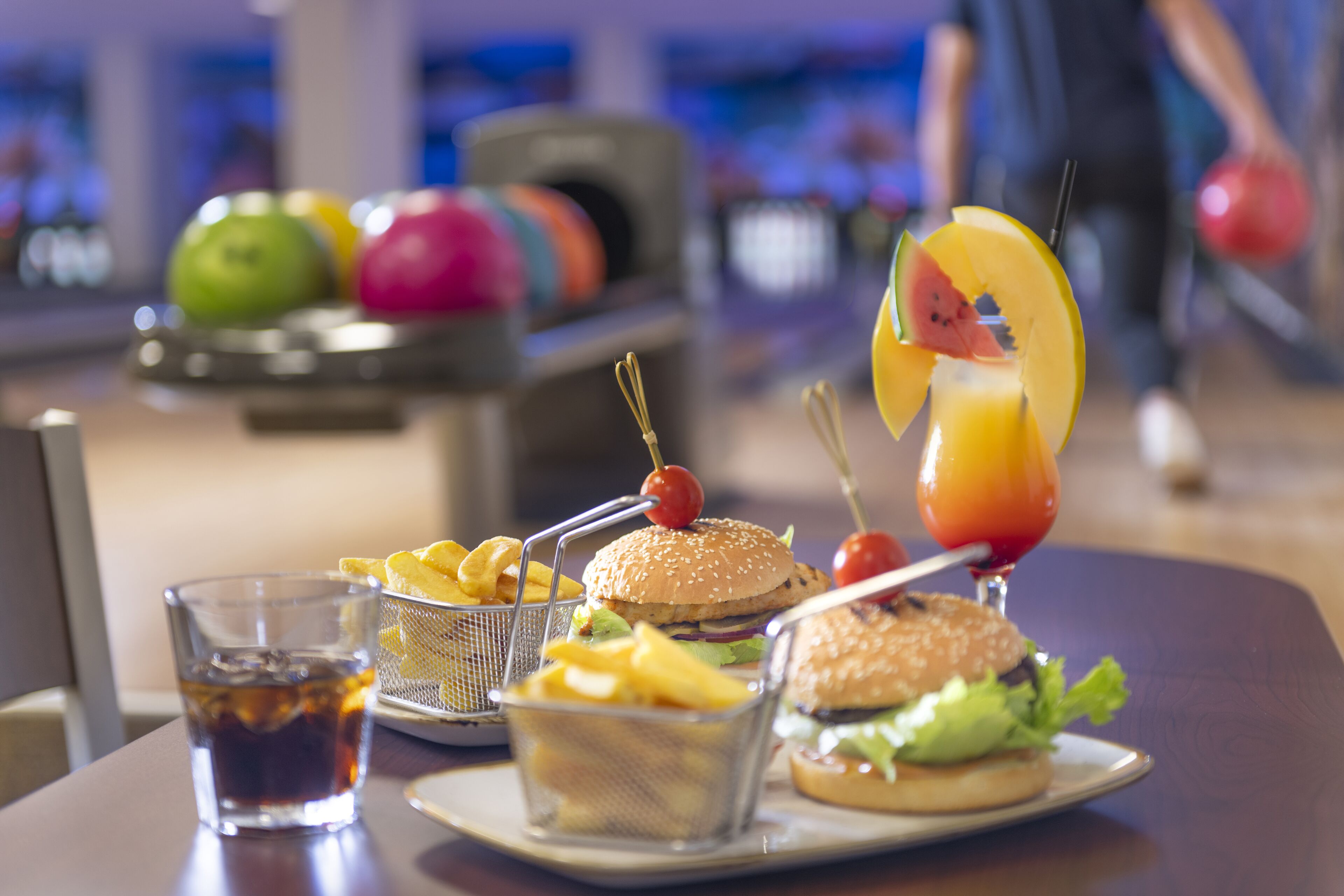 A dining table with a burger, fries, a drink, and a basket of chips.
