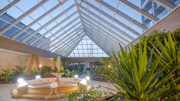 A spacious atrium with a glass ceiling, a central fountain, and lush greenery. - Olymp IV Spa & Wellness (Kolobrzeg)