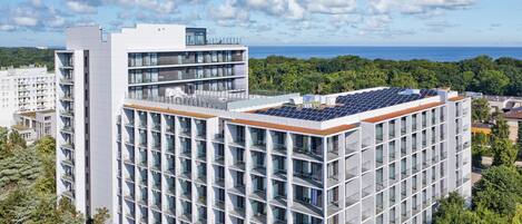 A modern multi-story building with a rooftop solar panel array, surrounded by greenery and a clear sky.