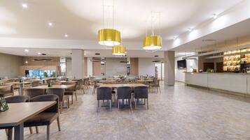 A spacious dining area with multiple tables and chairs, a bar area with a variety of beverages, and pendant lighting.