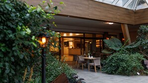 An outdoor patio area with a wooden bench, a table, and chairs. There are potted plants and a lamp post. - Olymp IV Spa & Wellness (Kolobrzeg)